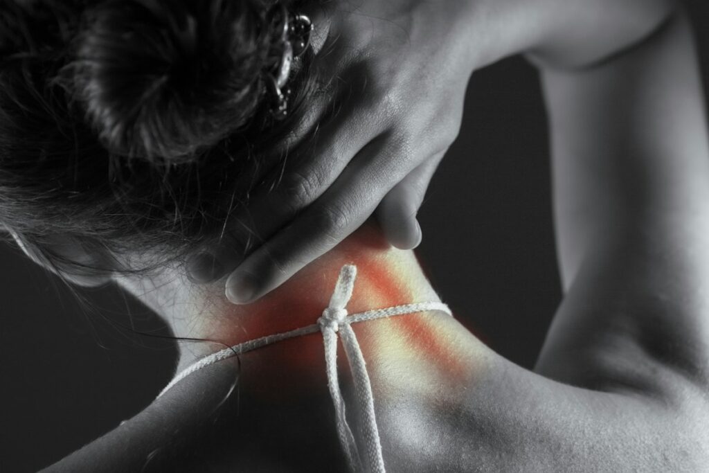 Mulher com mão sobre a região cervical em imagem que representa dor no pescoço